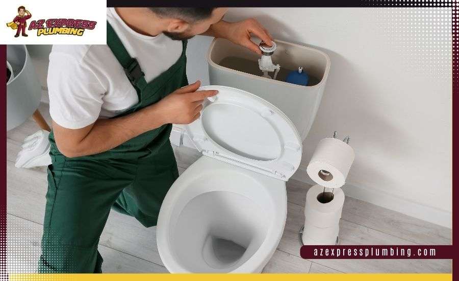 A plumber in green overalls repairs an open toilet tank in a modern bathroom, featuring AZ Express Plumbing branding.
