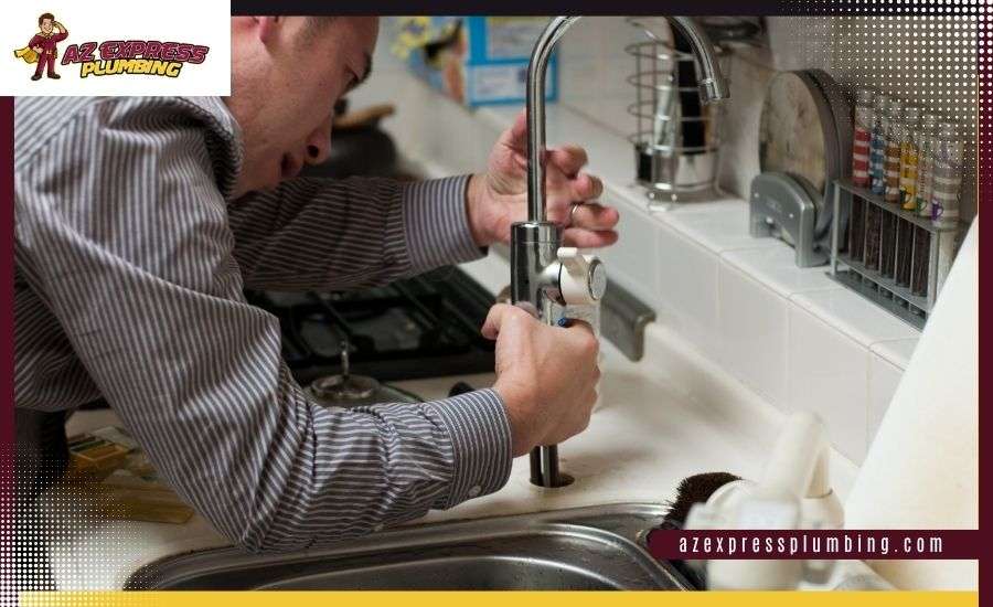 A man in a striped shirt using both hands to install or repair a tall metal kitchen faucet at a sink.